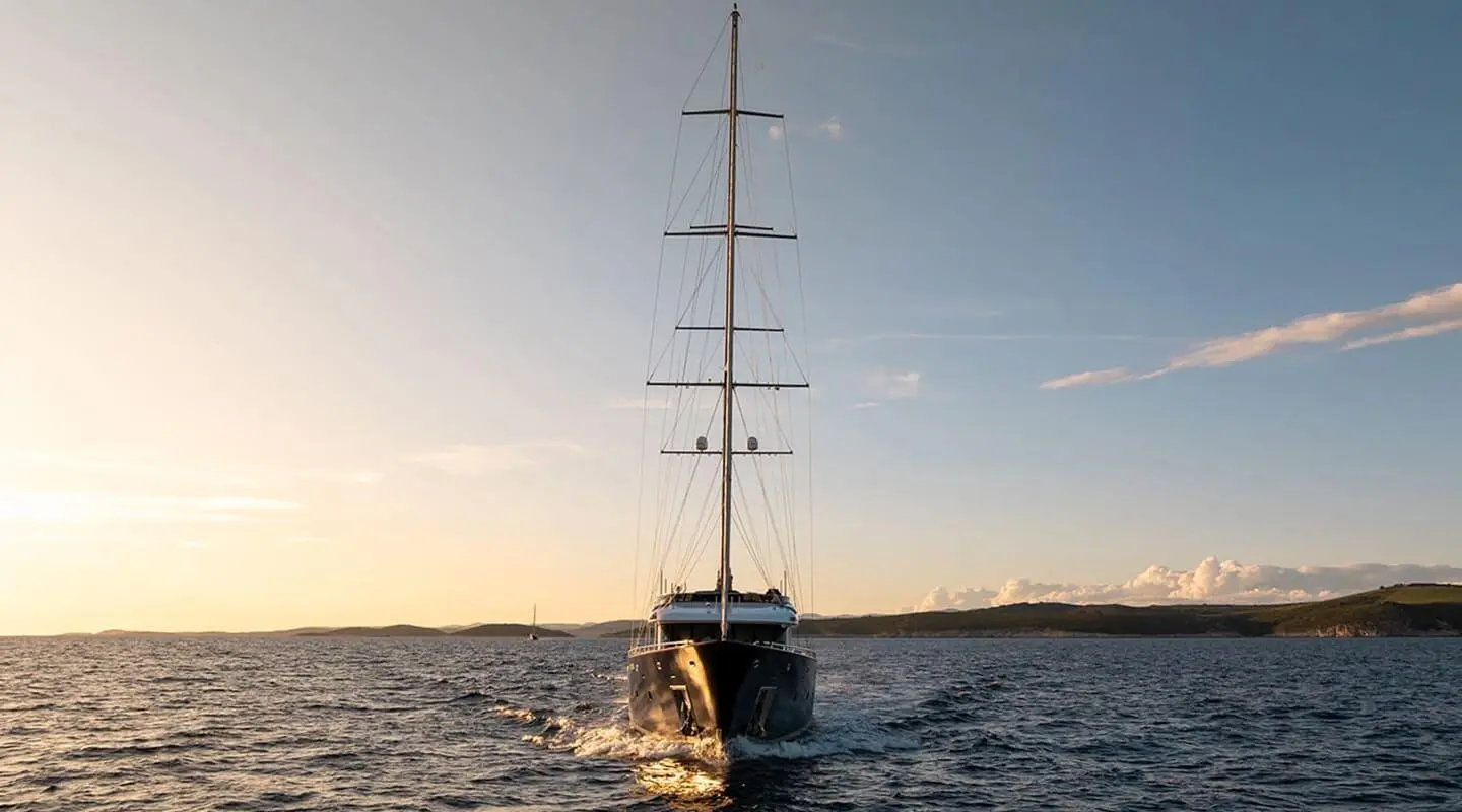 Yacht Dalmatino with tall masts sails in calm sea at sunset