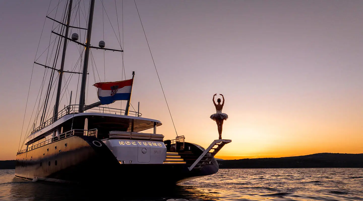 Nocturno yacht anchored at sunset with silhouette sails and calm water