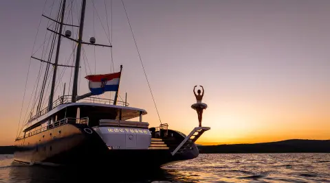 Nocturno yacht anchored at sunset with silhouette sails and calm water