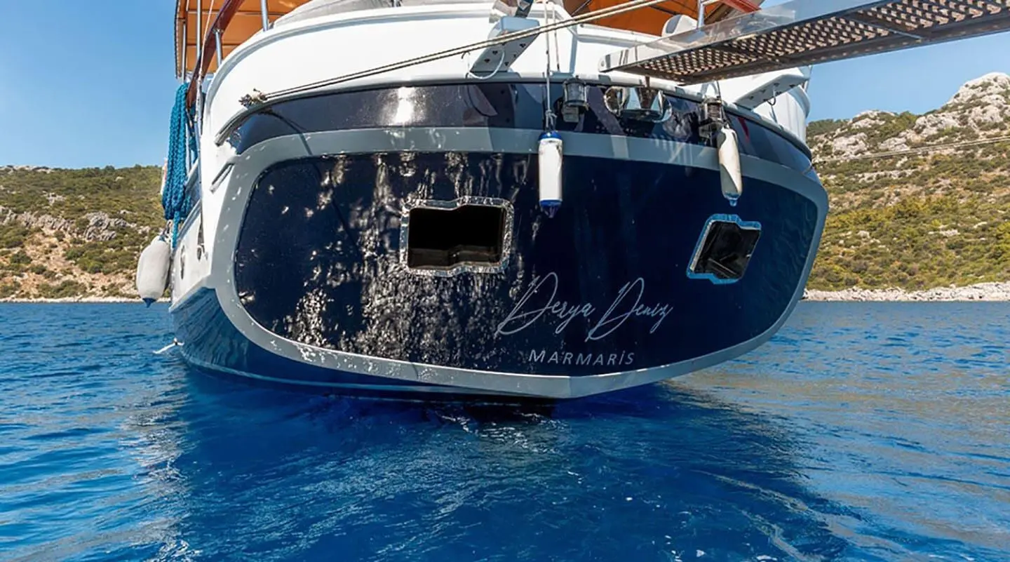 Wide view of a dark blue yacht anchored on calm blue water at sunset
