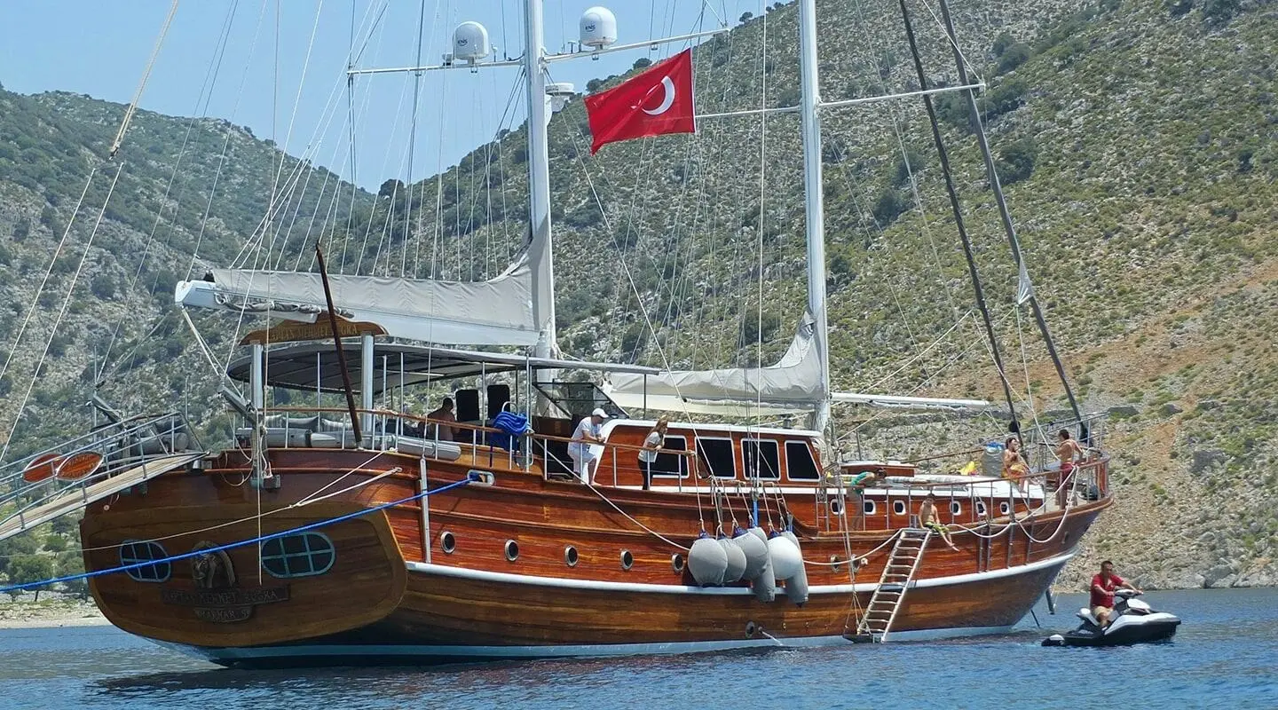 Wooden gulet yacht named Kaptan Mehmet Bugra sailing with sails up and Turkish flag