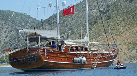 Wooden gulet yacht named Kaptan Mehmet Bugra sailing with sails up and Turkish flag