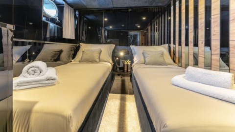 Two twin beds in a luxurious cabin interior with mirrored walls and curtains, a small center table with flowers