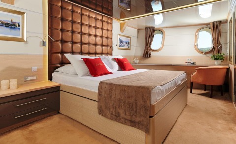 Bedroom on a yacht with a large bed, brown padded headboard and red cushions