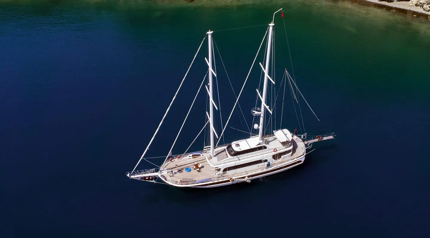 Kayhan 4 yacht anchored offshore with white sails and deep blue water