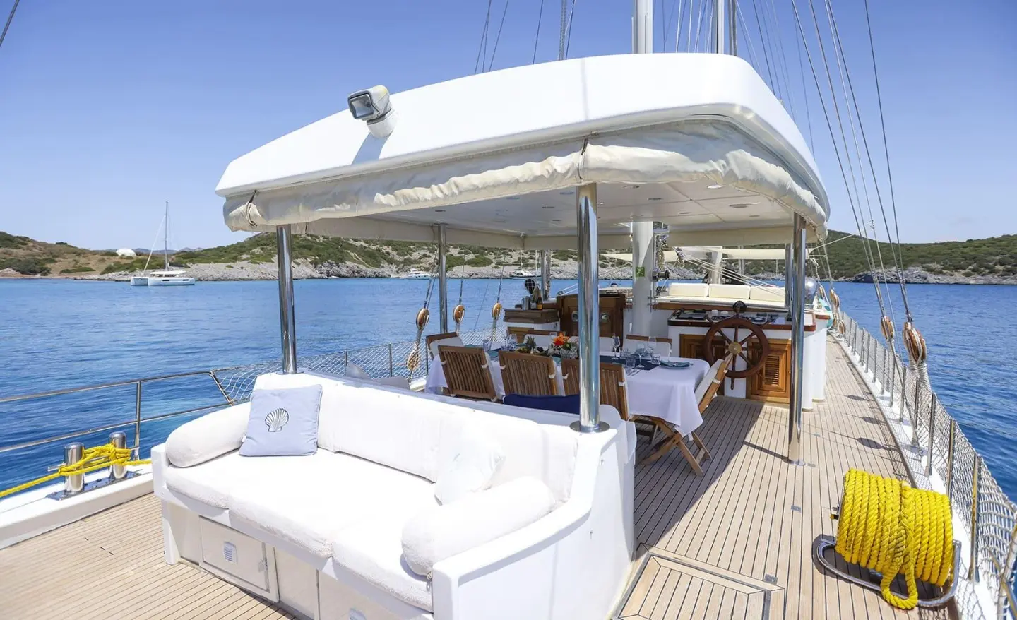Sunlit open deck with dining table and white seating on a yacht