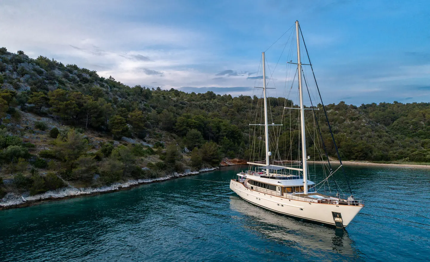 Navilux yacht anchored in turquoise cove beside forested hills and clear blue sky