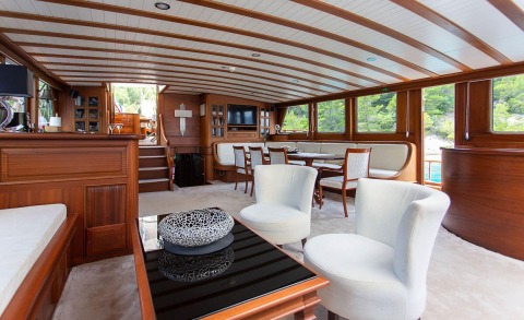 Dolce Vita luxurious yacht interior: polished wood paneling, white upholstered seating, and a glass-top coffee table in the salon