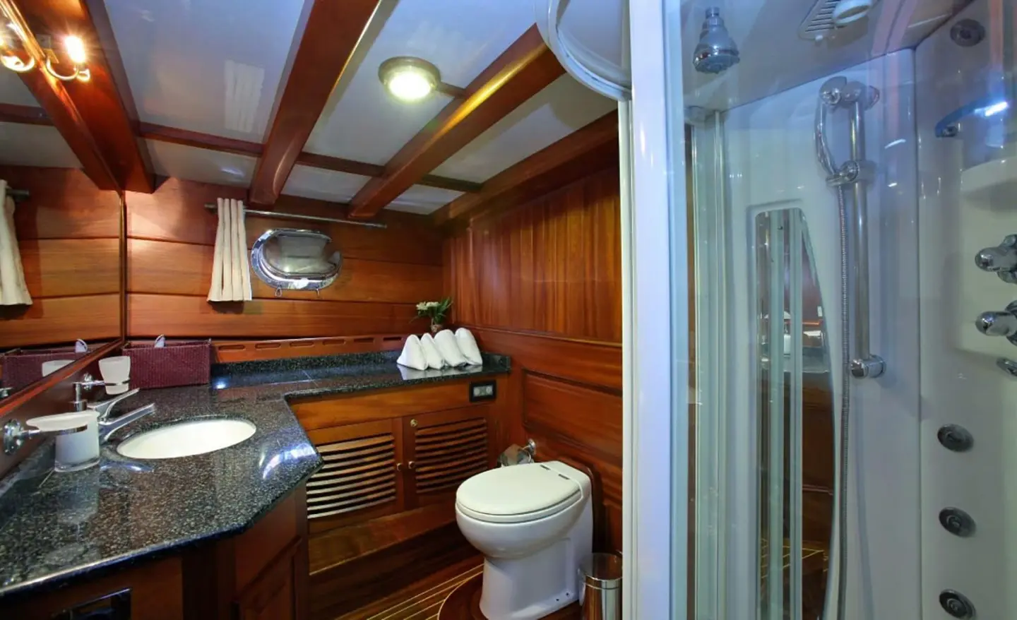Wood-paneled yacht interior with sink and glass shower enclosure