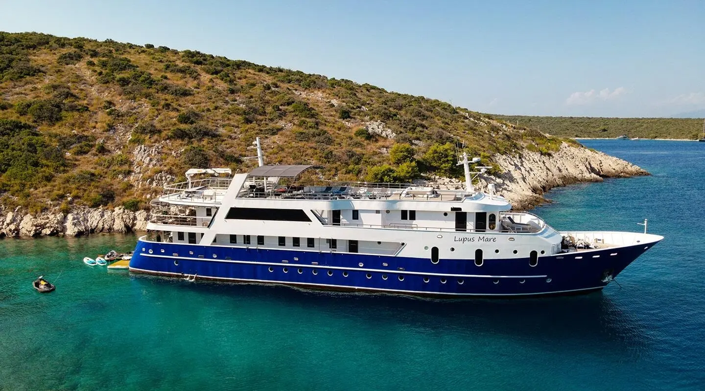 Lupus Mare luxury yacht anchored near rocky coastline with clear blue water