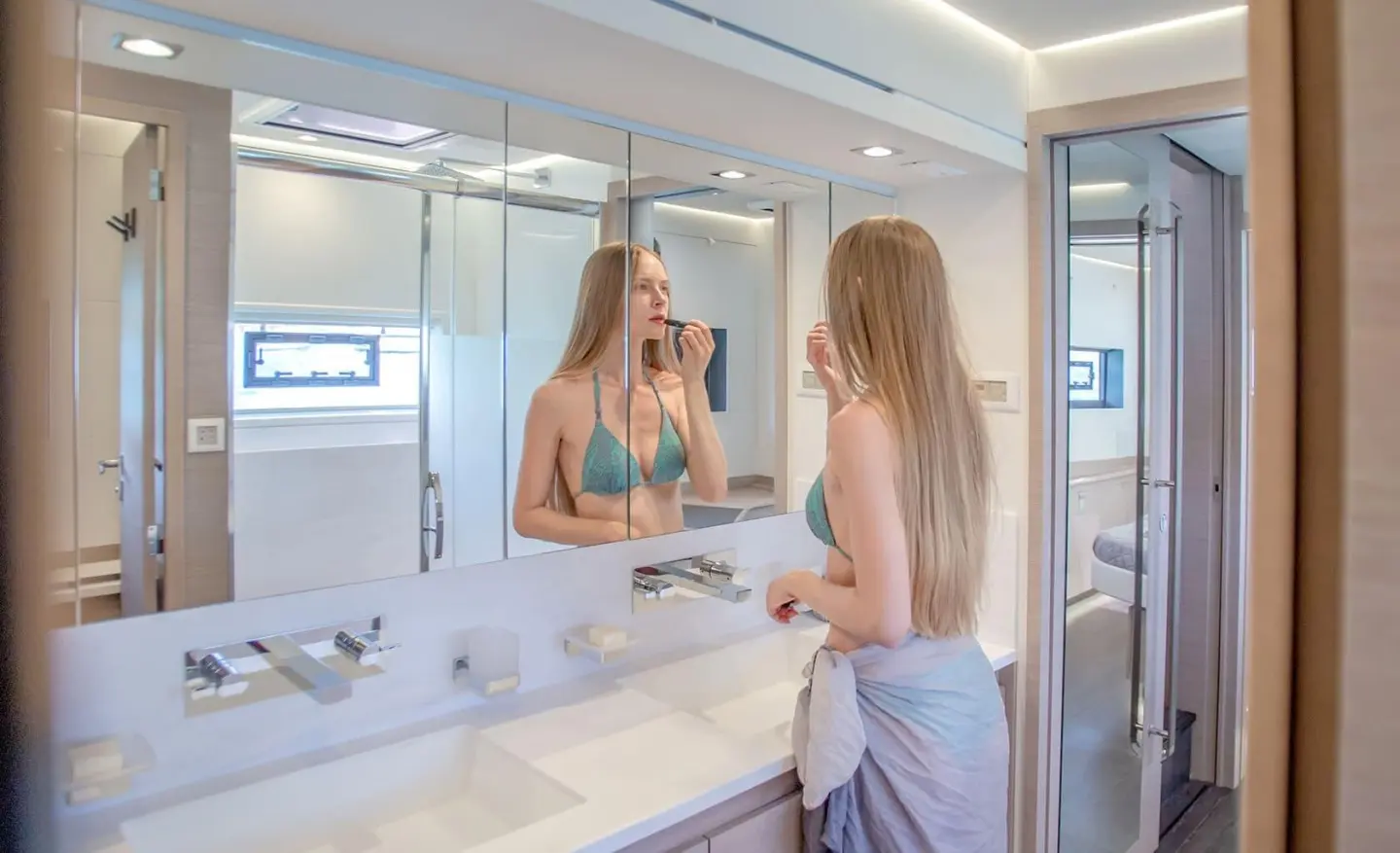 D2 luxury yacht bathroom with large mirror, white sink, and two women looking at reflections