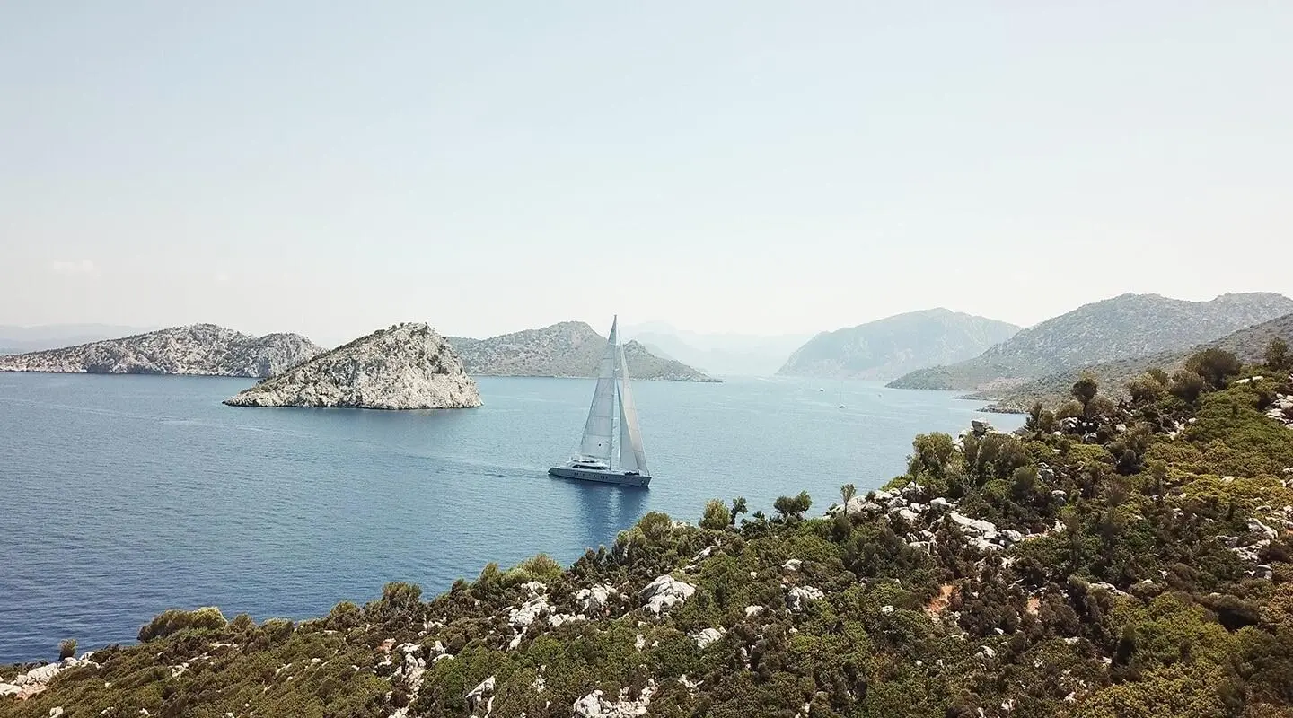 Silhouetted sailing yacht anchored in calm turquoise sea, rocky coastline