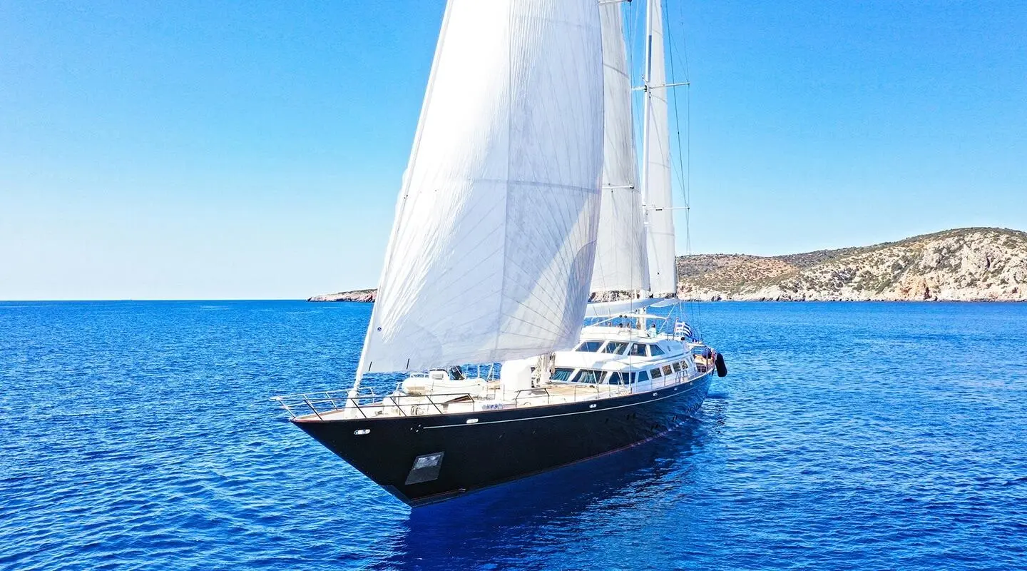 Yacht Tamarita sails afloat with white sails on blue sea under clear sky