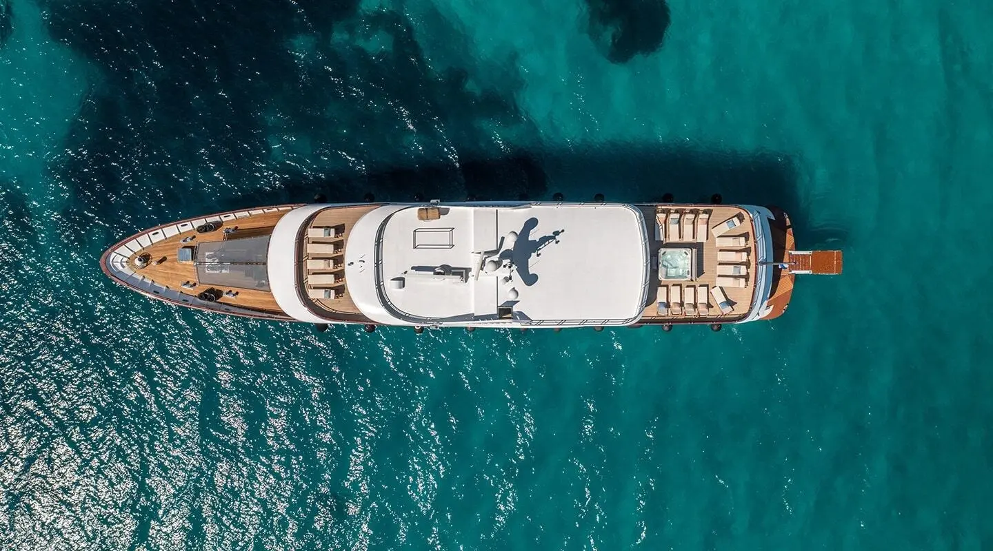 Overhead view of a white motor yacht named Olimp anchored in turquoise water