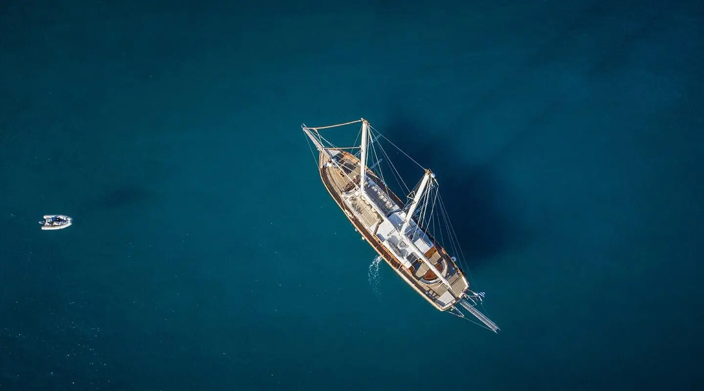 Small wooden yacht with sails at sea, viewed from above during calm blue water day