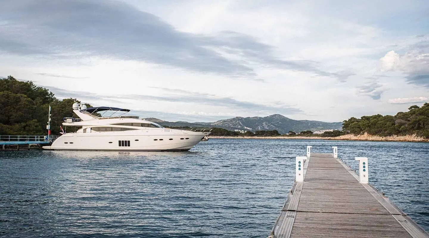 White large motor yacht docked at a marina with a pier in the foreground