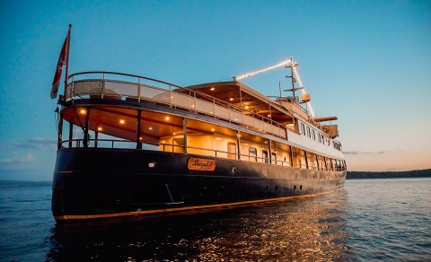Seagull II yacht at dusk with lit decks, dark hull and open upper deck