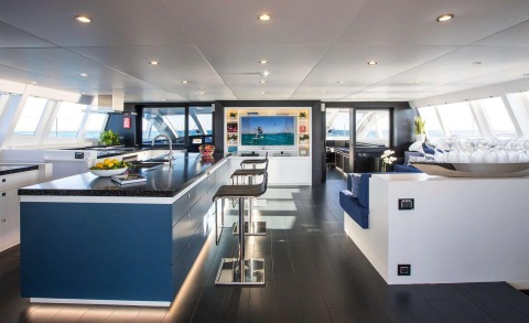 Luxurious yacht interior with kitchen island and seating, TV in the center and sea view outside
