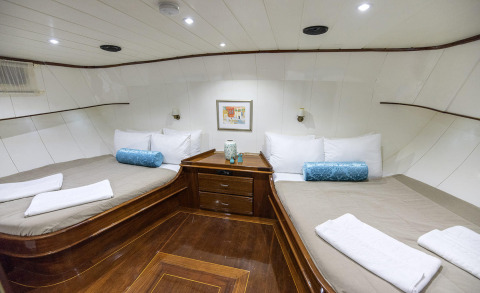 Interior of a yacht with two long beds, white pillows, and a wooden nightstand