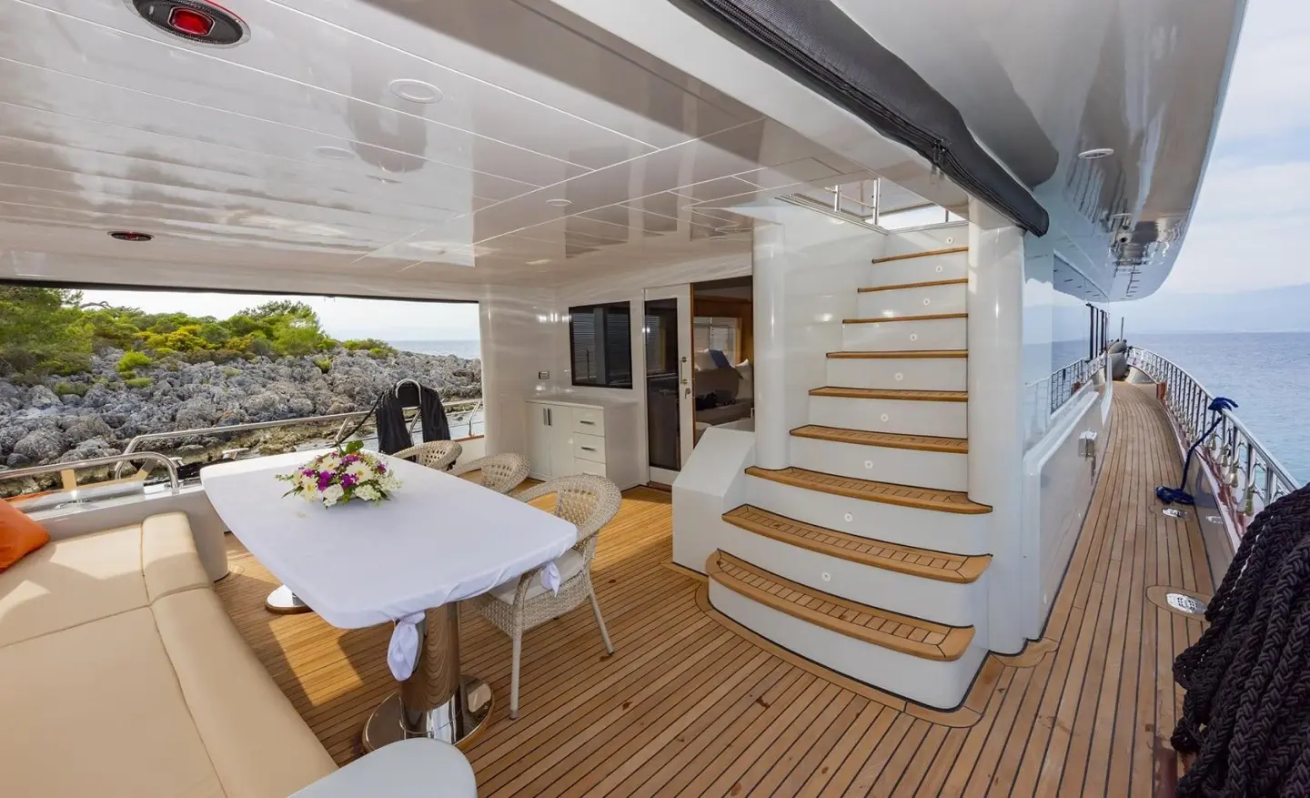 Yacht Simay M deck dining area with table, chairs, and curved stairs nearby