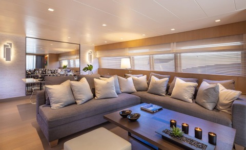 Interior yacht lounge with gray sofa and white cushions, coffee table with candles and decor, large mirror and blinds along window