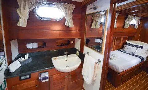 Inside a luxury yacht cabin with wooden panels, sink, mirror, and bed