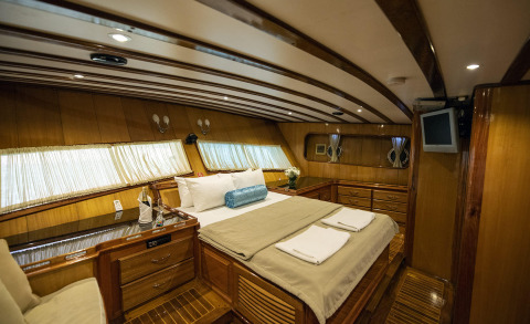 Kayhan 5 luxury yacht interior: master cabin with beige bedding, white pillows, blue bolster, wood paneling, and polished cabinetry