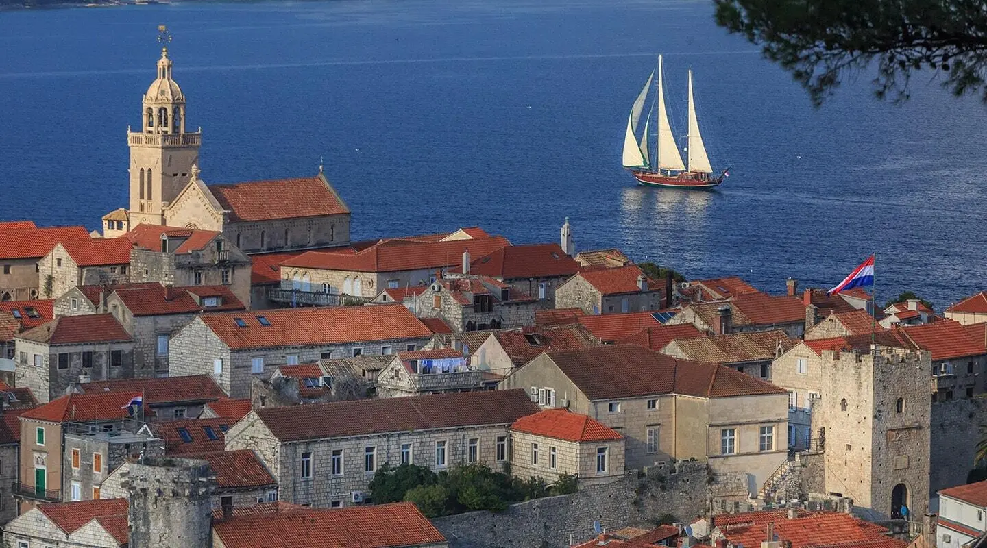 Gulet Carpe Diem 7 sailing near a coastal town with orange rooftops