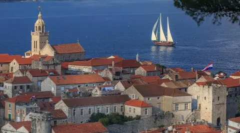 Gulet Carpe Diem 7 sailing near a coastal town with orange rooftops