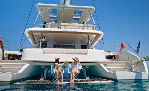Two people stand on the stern of a luxury white yacht named Daiquiri, water around