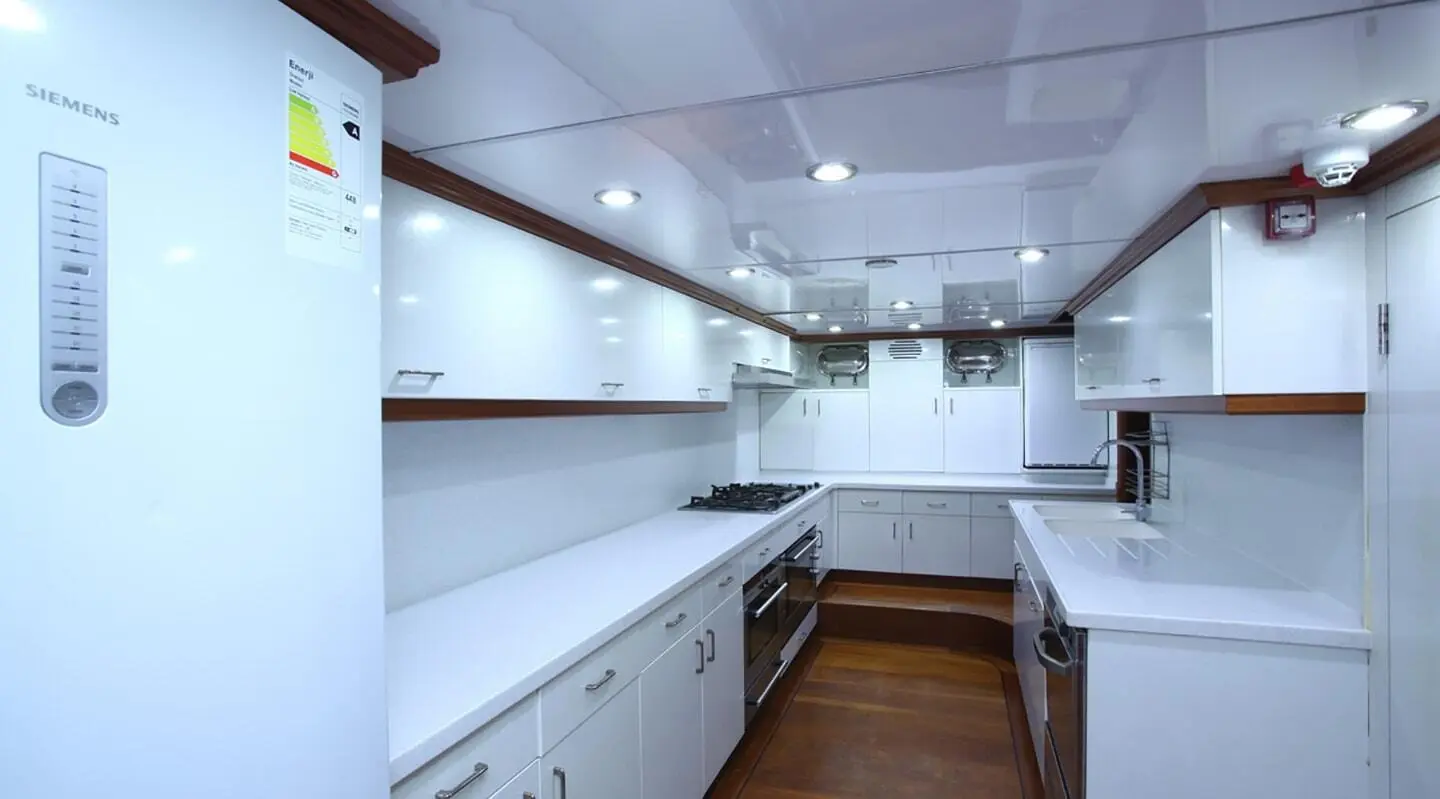 White galley with cabinets and countertops on a yacht, viewed from the corridor