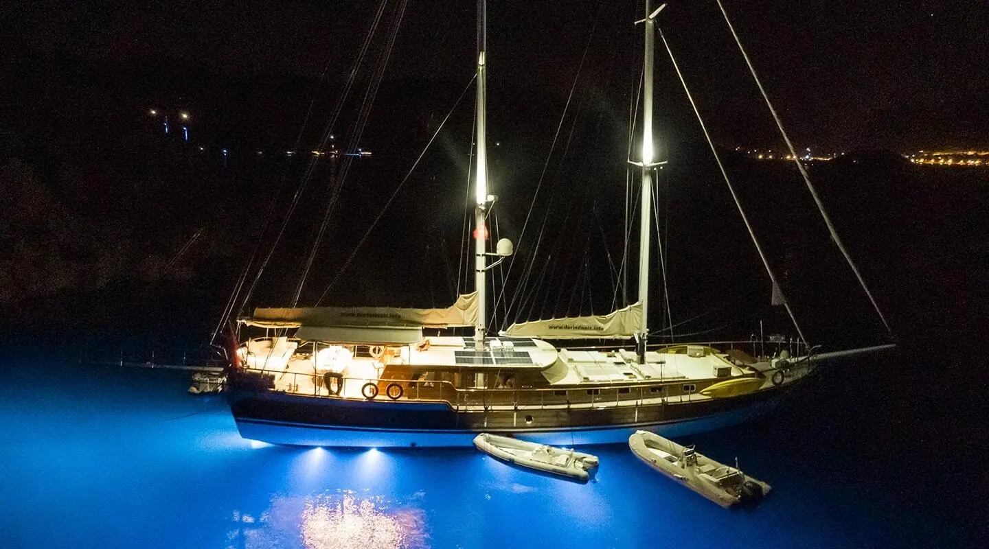 Derin Deniz yacht at night, illuminated by lights, moored beside a dark sea
