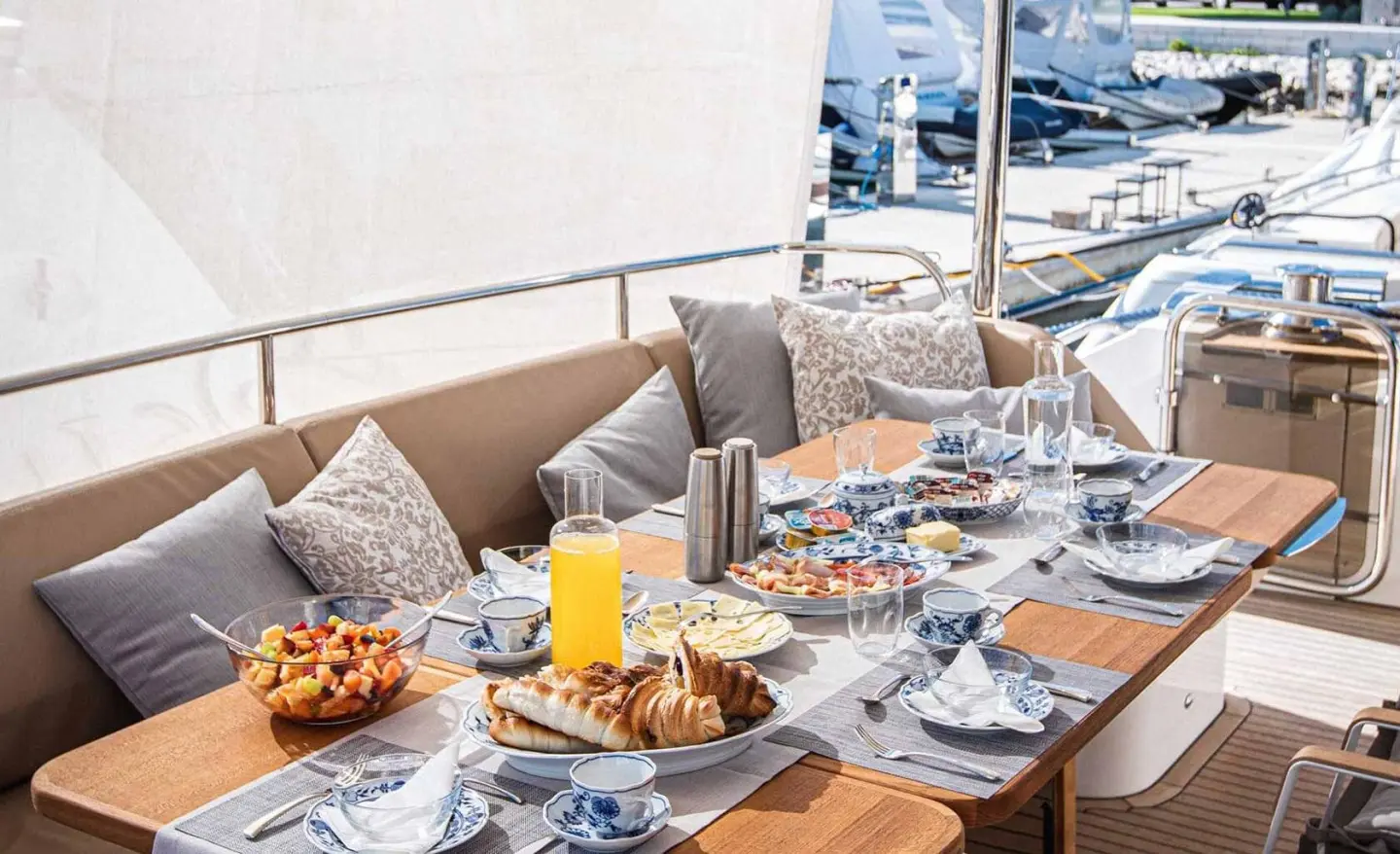 Open deck dining area on a yacht with table set for breakfast and pastries