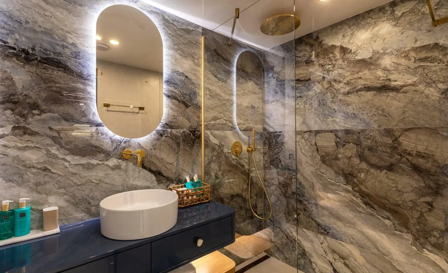 oval backlit mirror, gold fixtures and glass shower in marble bathroom