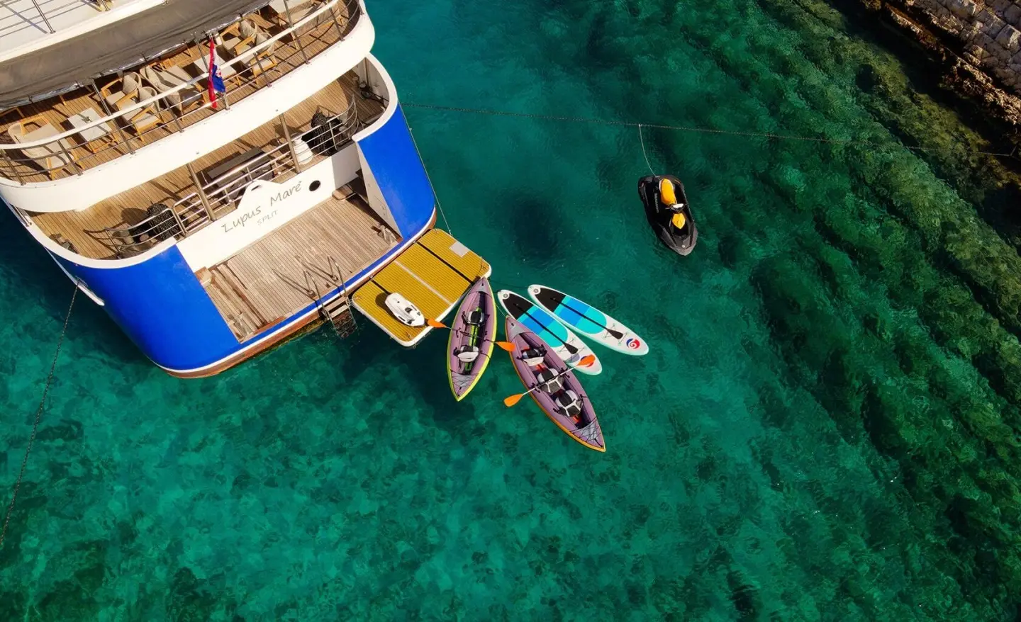 Lupus Mare yacht docked at sunset with swimmers in clear turquoise water