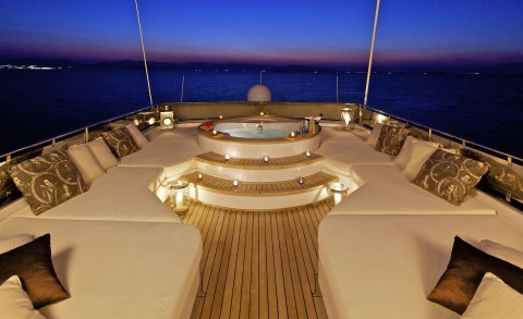 Open aft deck with seating around a central hot tub and sunset view on a luxury yacht