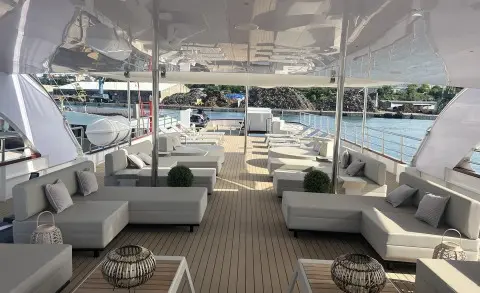 Salon on Melody yacht with white cushioned seating and teak deck under a covered area