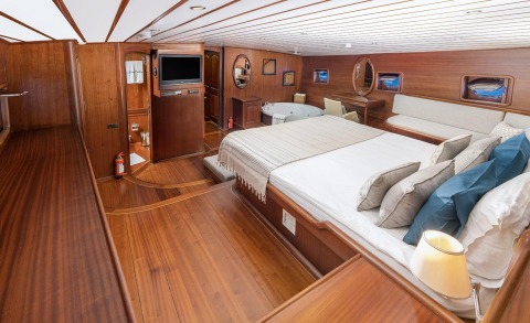 Wood-paneled cabin with a large bed and sofa area inside a yacht