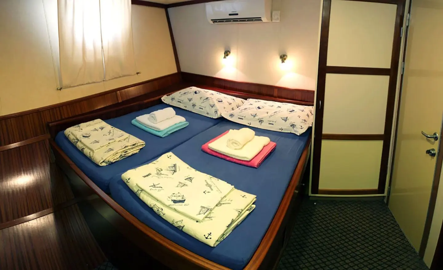 Tajna Mora yacht cabin with blue bedding, red pillows, and towels folded