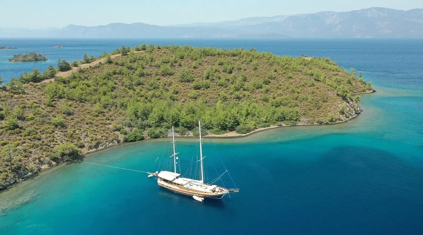 Enderim A yacht anchored near a lush green coastline at sunset, calm turquoise sea