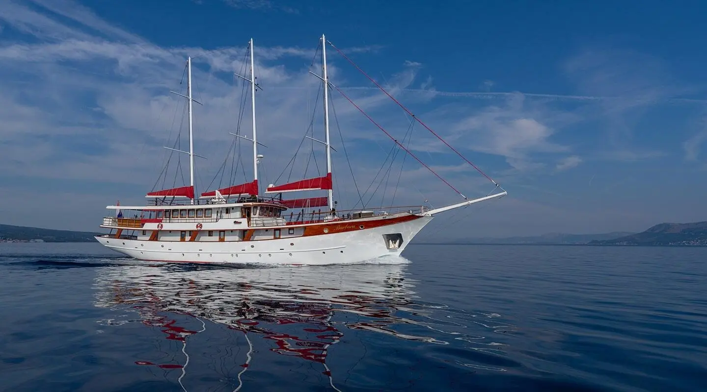 White motor-sailer yacht with red sails on calm sea