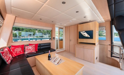 Interior salon with wood furniture, black leather sofa and red patterned cushions, large window with outdoor view