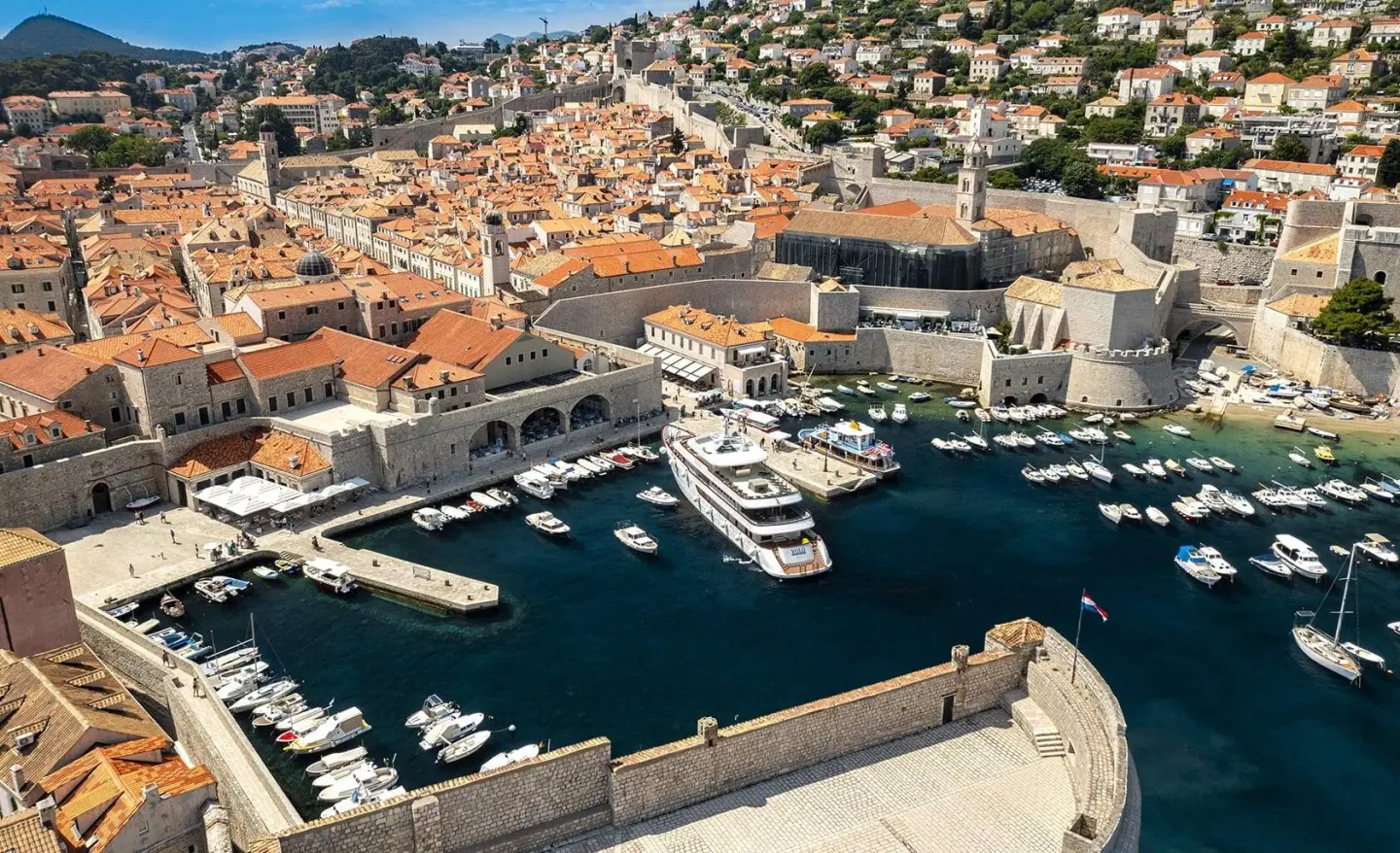 Large white yacht in Dubrovnik harbor with the old stone city walls nearby
