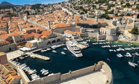 Large white yacht in Dubrovnik harbor with the old stone city walls nearby