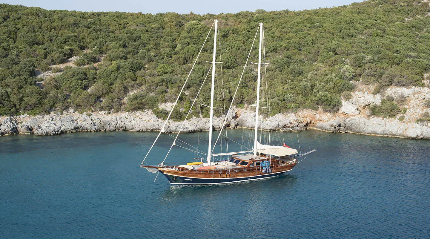 Samarkand yacht sailing near rocky coastline at sunset with masts and sails