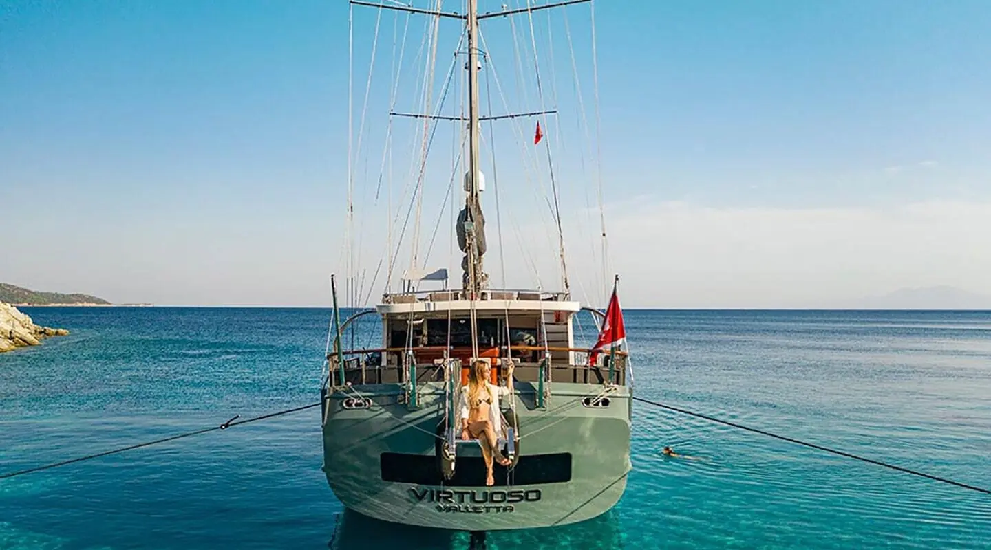Virtuoso yacht anchored at sunset with passengers on stern, calm blue sea