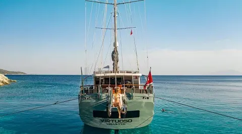 Virtuoso yacht anchored at sunset with passengers on stern, calm blue sea