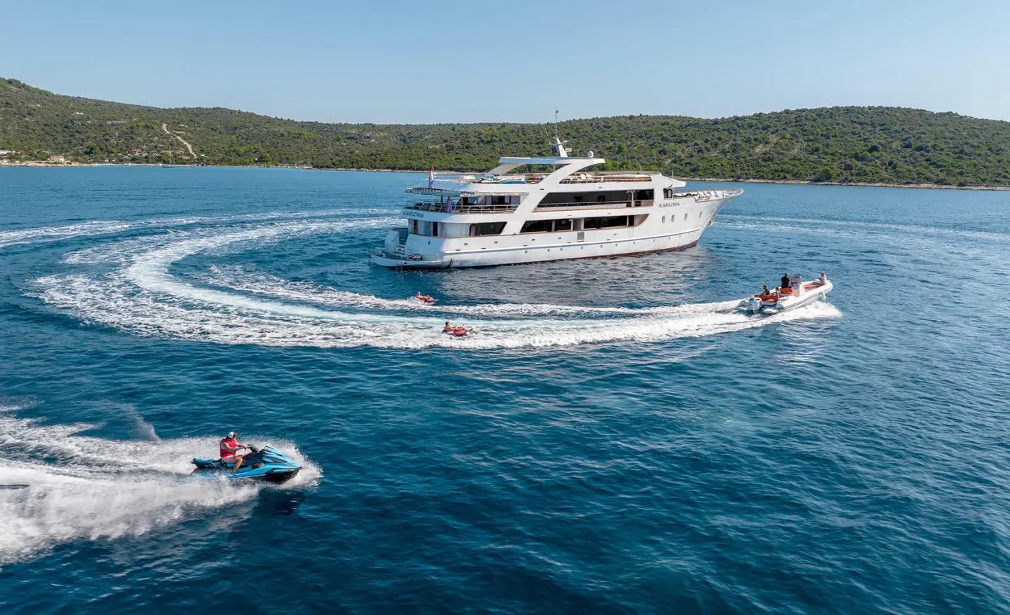 Yacht Karizma cruising on blue water with a small dinghy nearby