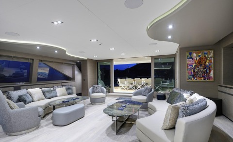 Modern indoor lounge area with curved sofas, ottomans, and glass doors opening to the outside deck at night