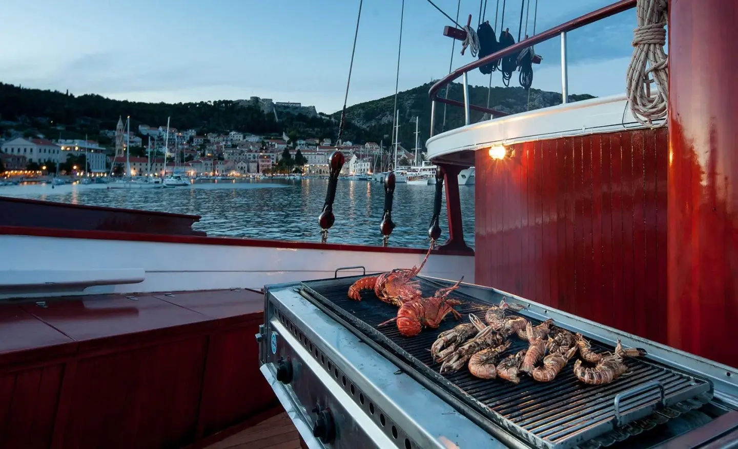 Romanca yacht aft grill on deck with coastal town in background at dusk
